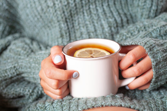 Person holding a cup of tea with lemon slice