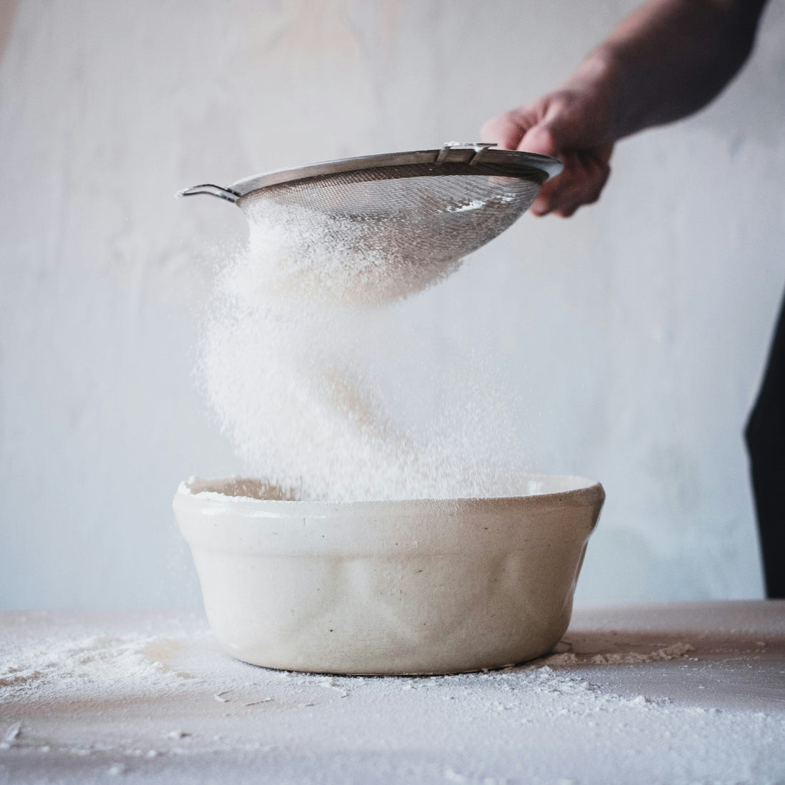 person sieving sugar into a bowl